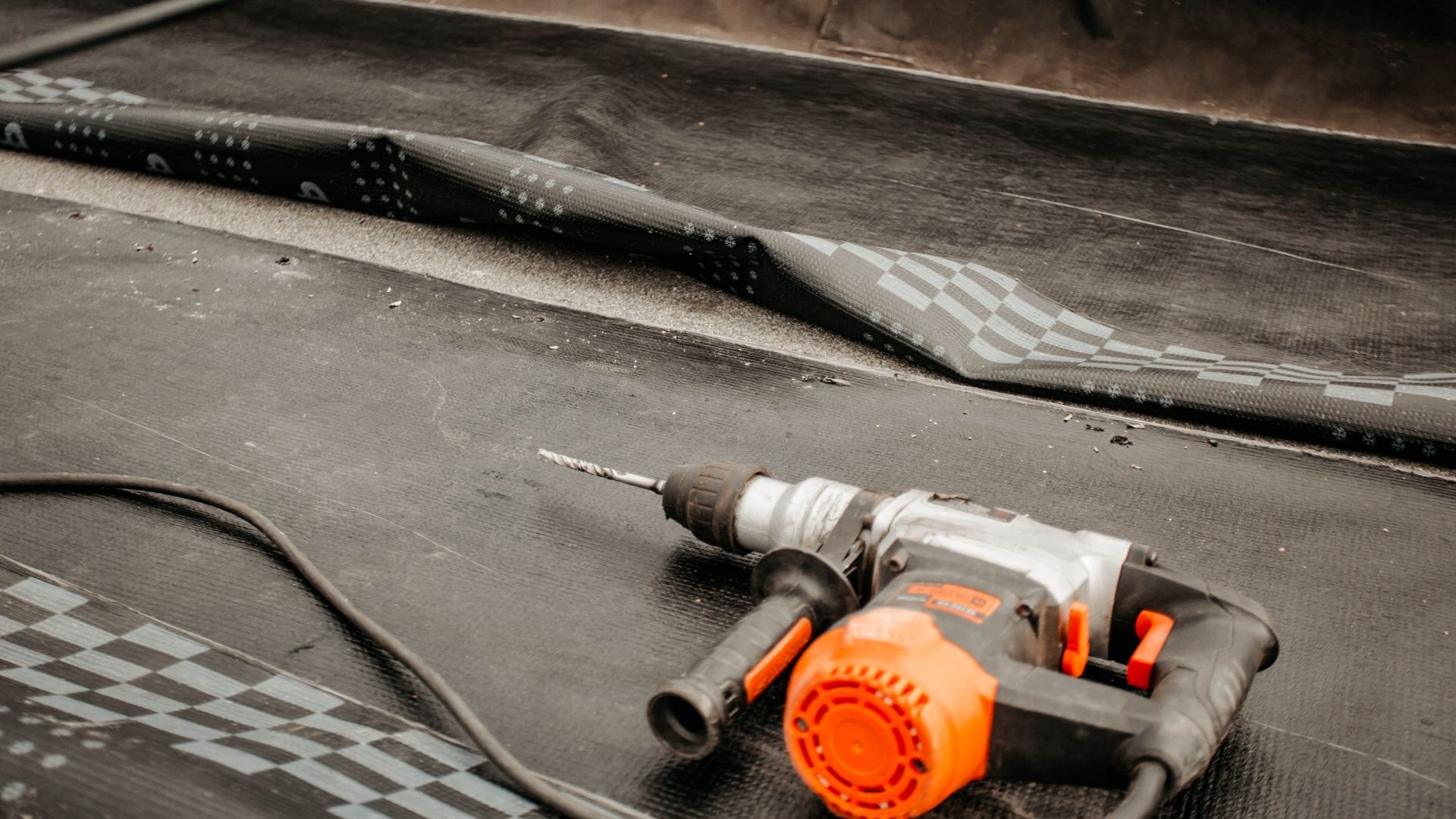 Orange and gray power drill on textured surface with carbon fiber background