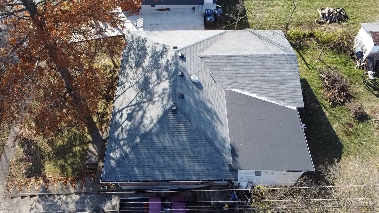 Aerial view of a gray shingled roof with tree shadows in autumn