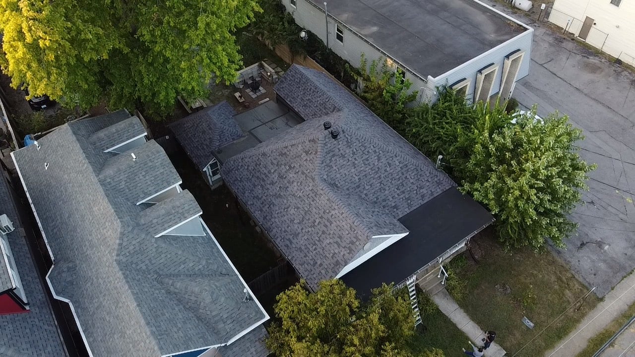 Aerial view of residential rooftops with gray shingles and surrounding trees