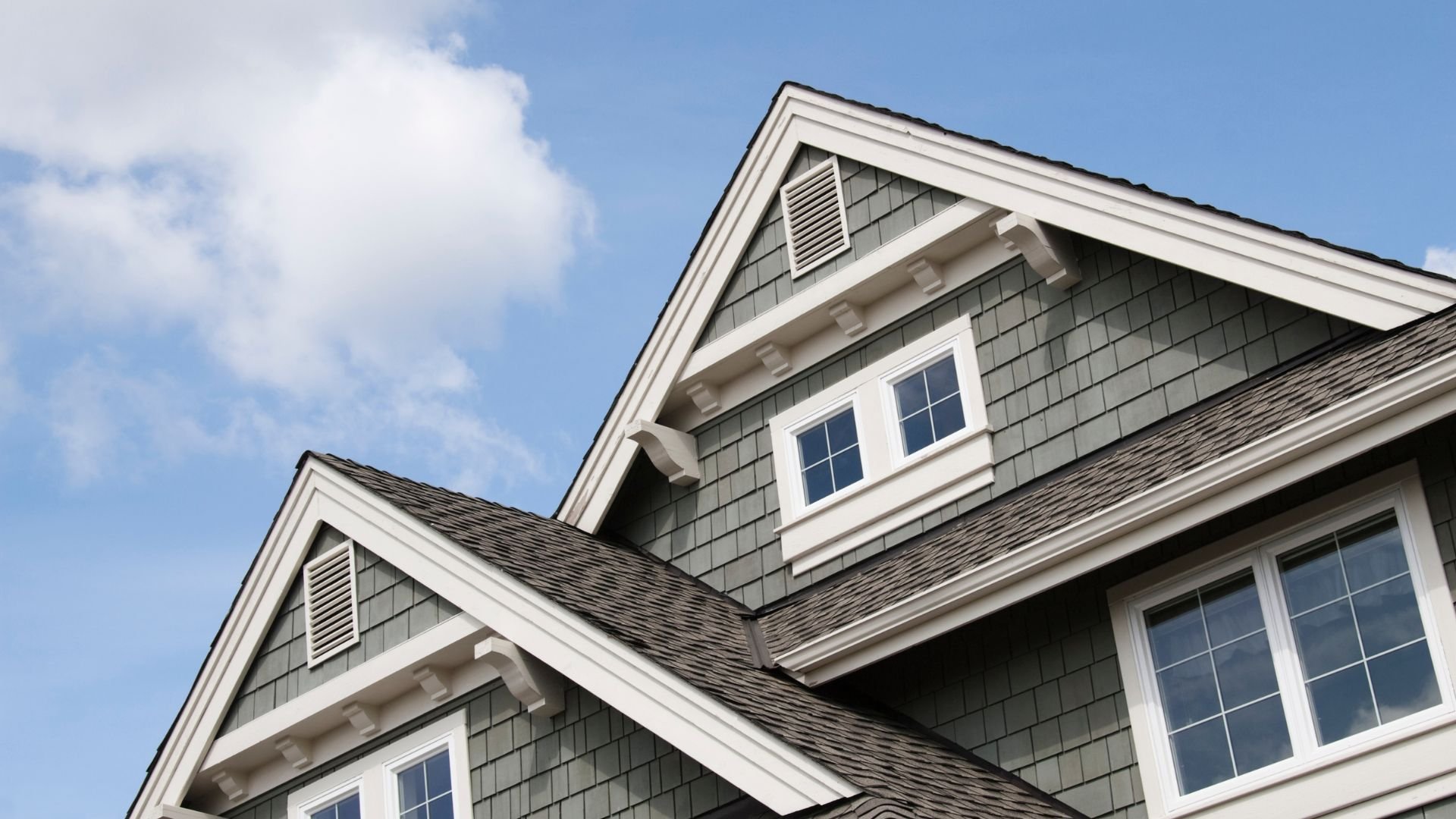 Gray shingled house with white trim under blue sky with clouds